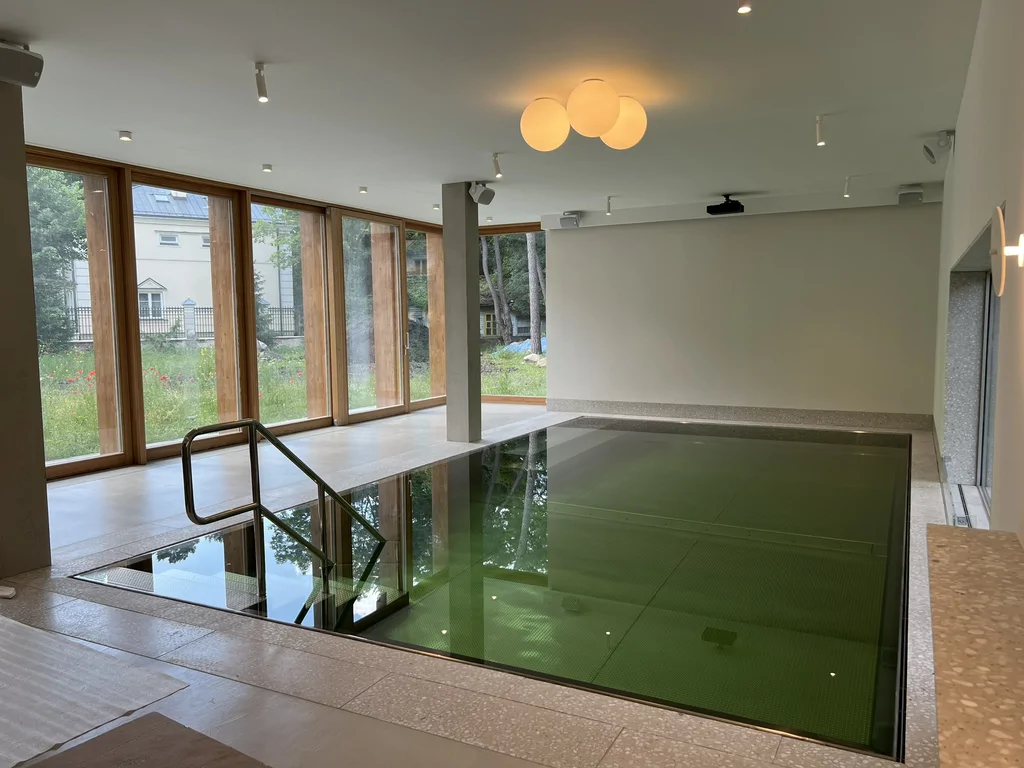 Wewnętrzny basen z dużymi przeszkleniami, betonowym słupem i widokiem na ogród