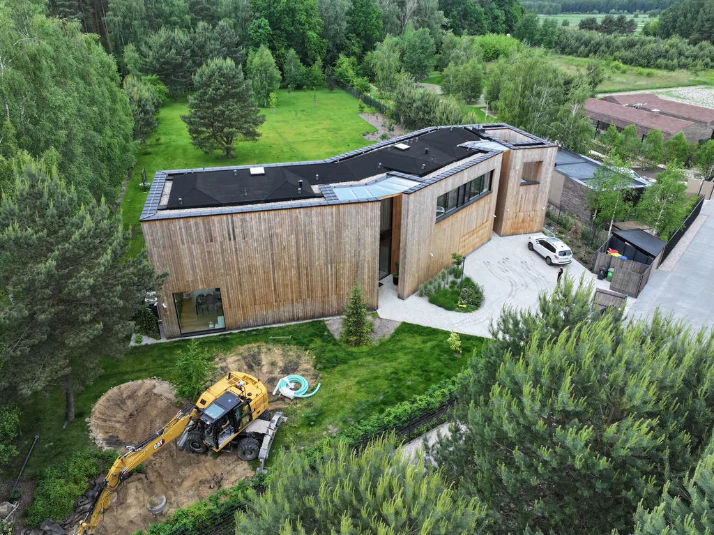 Dom Prawdziwka w otoczeniu lasu – widok z drona na bryłę budynku, podjazd i teren ogrodu.