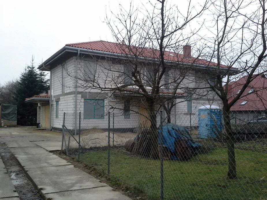 Budowa Domu jednorodzinnego widok z zewnątrz, wykonane mury oraz elementy konstrukcyjne; gotowy dach zaślepione otwory okienne