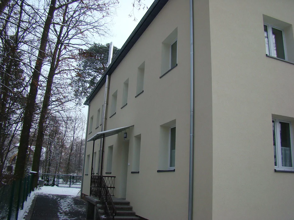 Elewacja boczna budynku po remoncie w zimie; wejście ze schodami i rzędem okien.