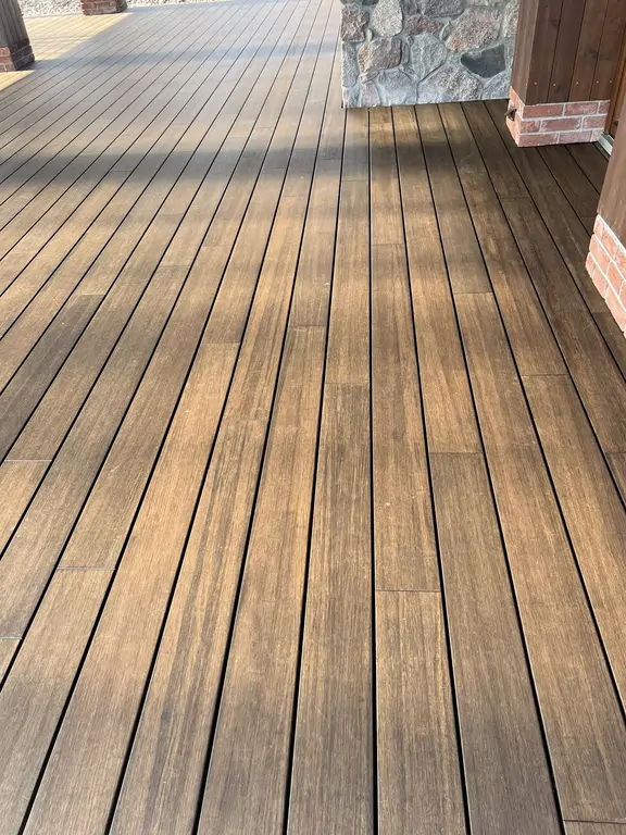 Detal wykończenia tarasu po remoncie z drewnopodobnymi deskami, kamienną ścianą i słupem obłożonym drewnem.