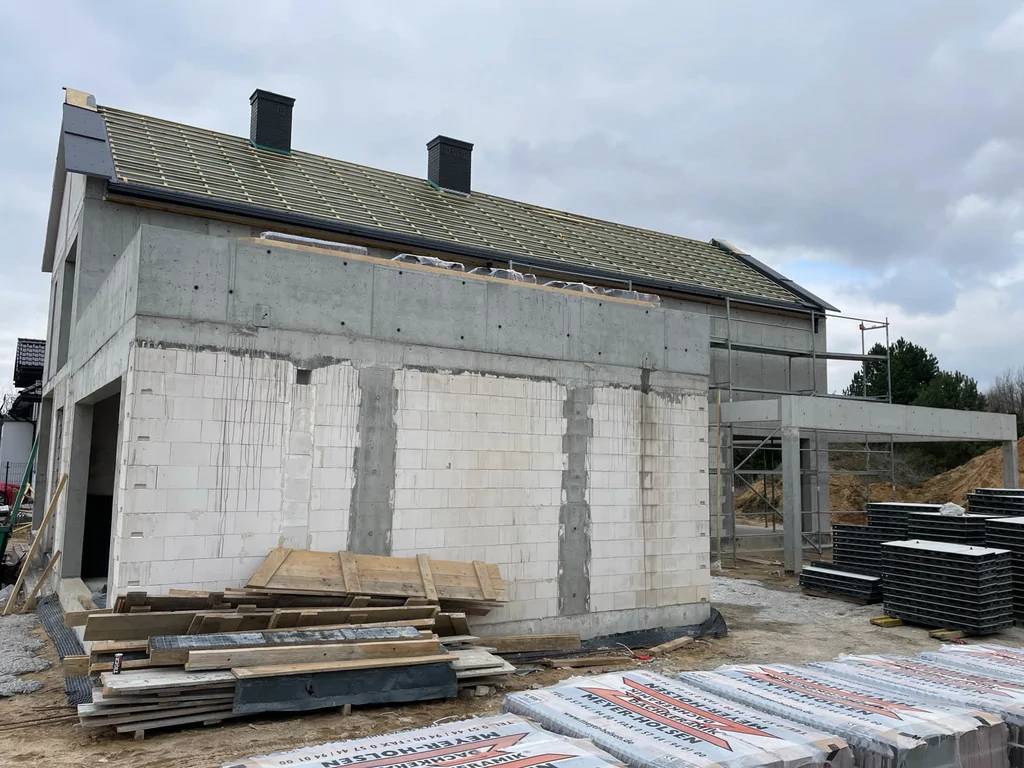 Boczna elewacja domu w stanie surowym z żelbetową konstrukcją, ścianami murowanymi i przygotowanym dachem skośnym