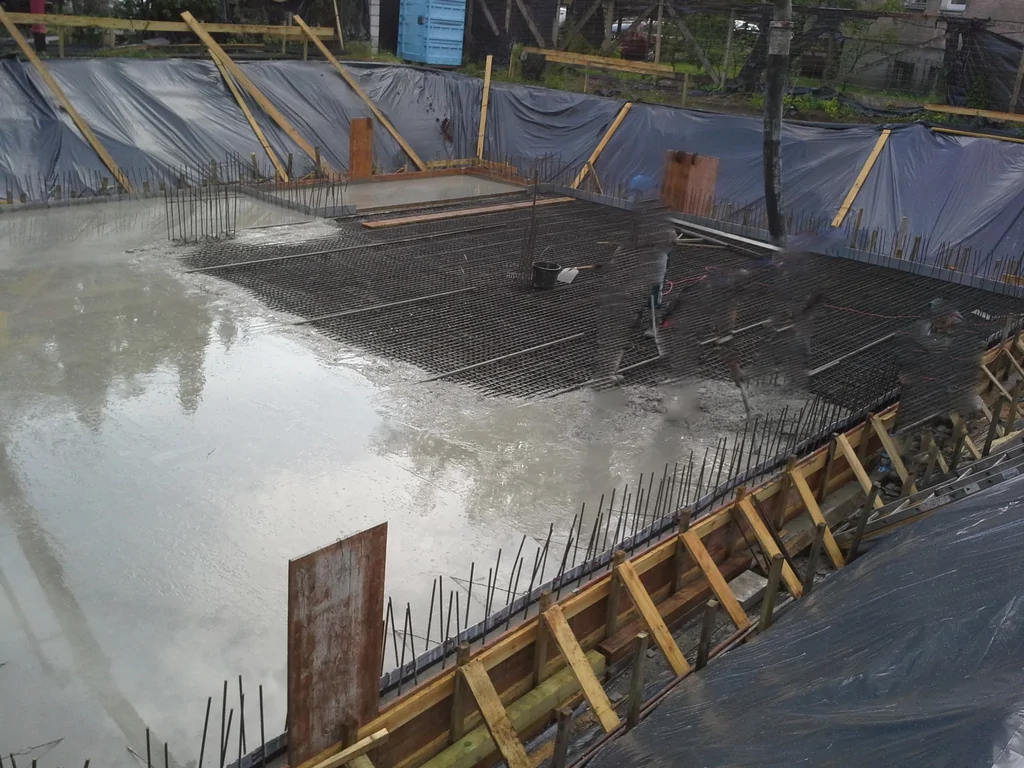 Budowa domu jednorodzinnego, widok na zbrojenie i wylewanie płyty fundamentowej piwnicy, biała wanna