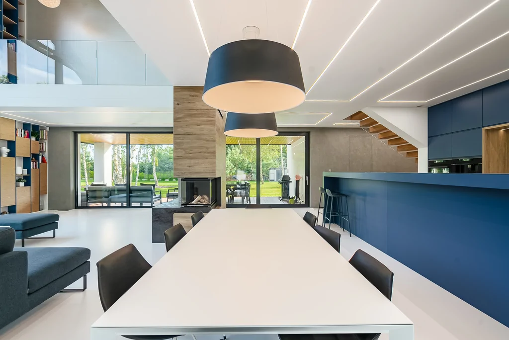 Jadalnia z białym stołem i czarnymi lampami w otwartej strefie dziennej.