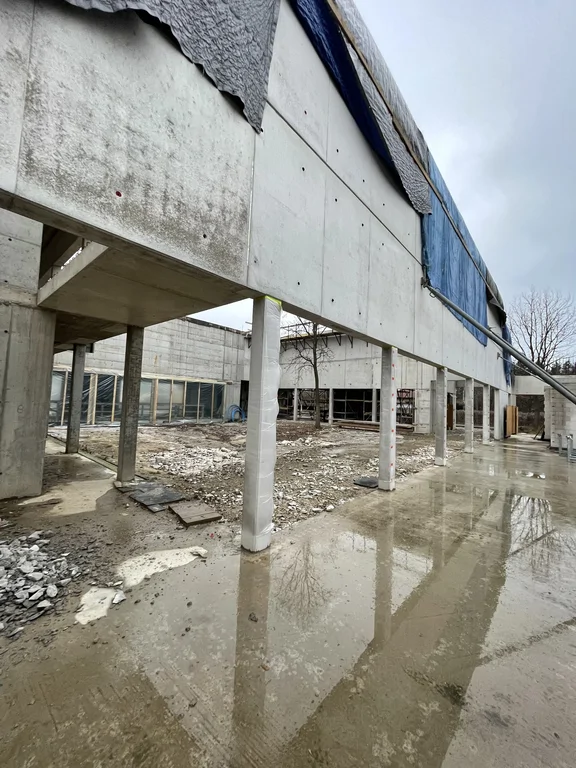 Podcień z żelbetowymi słupami i ścianą z betonu architektonicznego – widok na dziedziniec w stanie surowym.