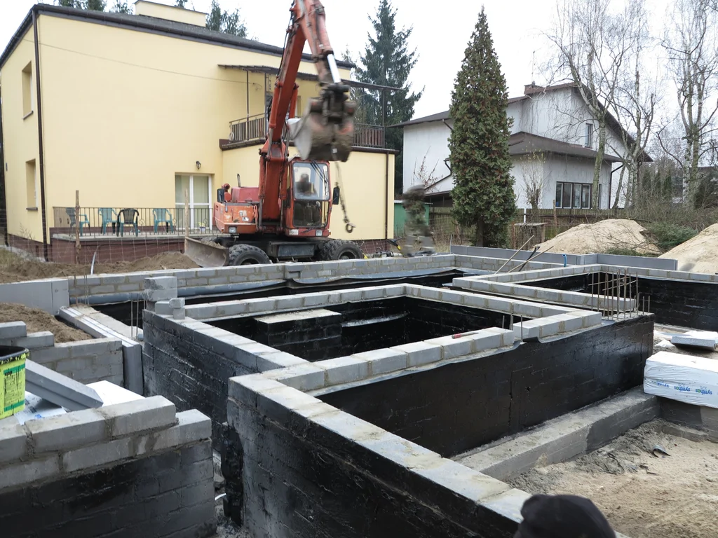 Budowa domu jednorodzinnego widok na wykonane fundamenty - ławy i ściany z bloczków betonowych w tle koparka 
