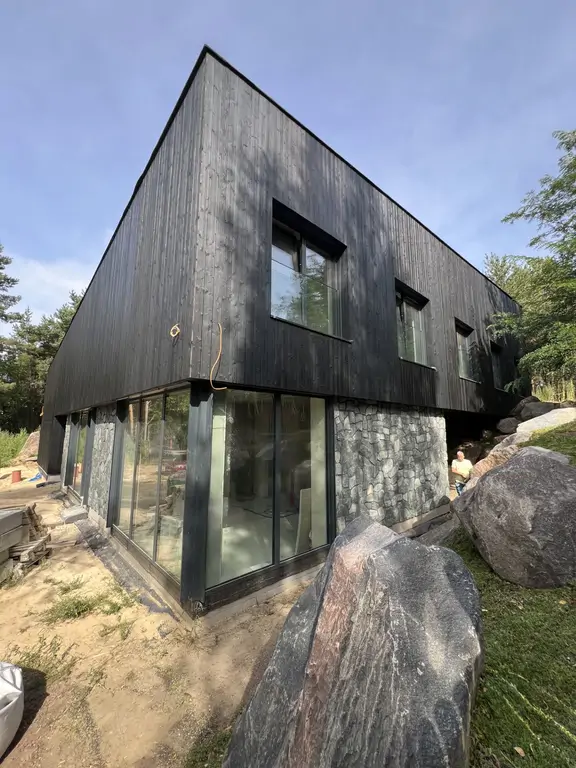 Widok z góry na wewnętrzny dziedziniec nowoczesnej willi z czarną elewacją drewnianą, przeszkleniami i kamienną skarpą.