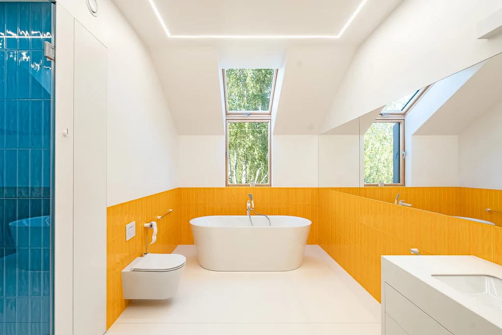 Nowoczesna łazienka z wolnostojącą wanną, pomarańczową okładziną ścian i dużym lustrem.
