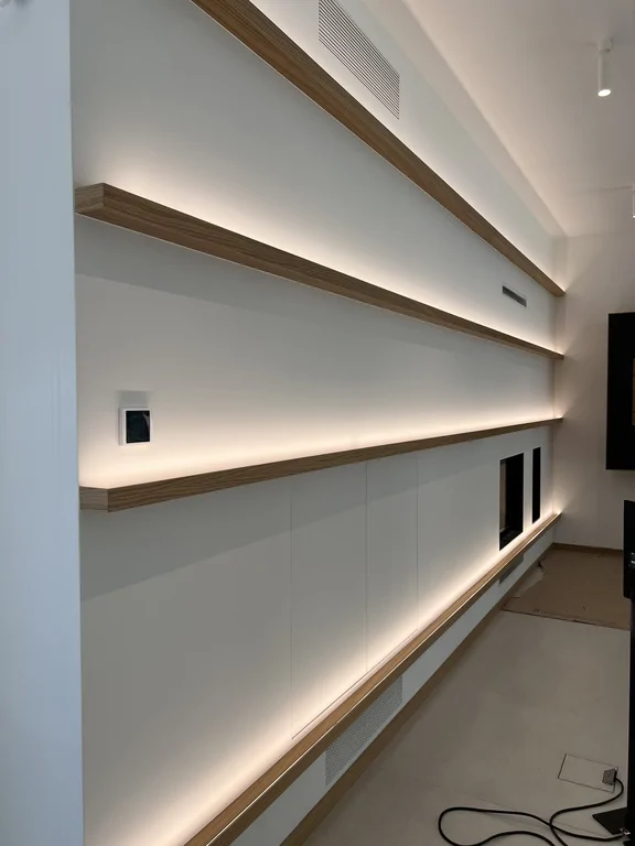 Podświetlana zabudowa ścienna w salonie z drewnianymi półkami i nowoczesnym kominkiem