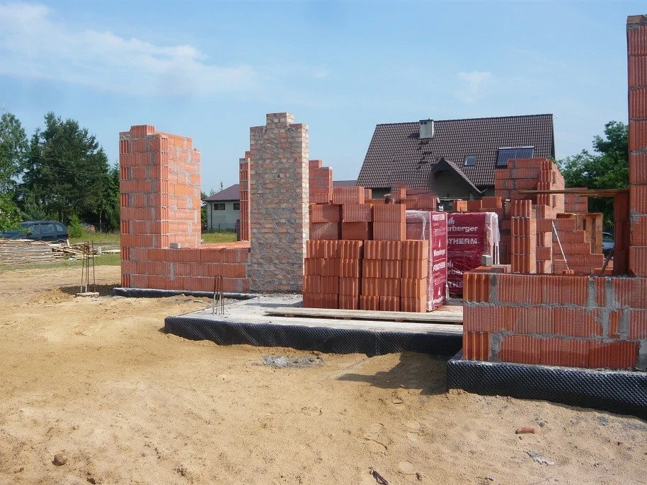 Wznoszenie ścian nośnych i komina, składowane pustaki i materiały na placu budowy
