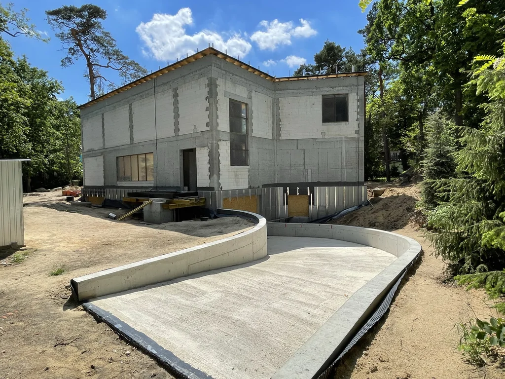 Betonowy zjazd do garażu podziemnego przy domu jednorodzinnym ze szczelną piwnicą wykonanej w technologii białej wanny.