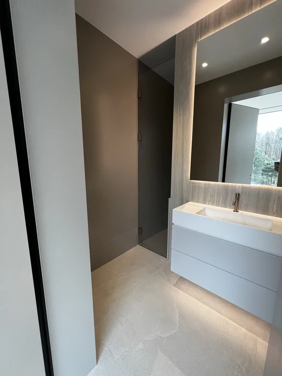 Strefa umywalki i prysznica w łazience: wielkoformatowe okładziny, lustro z LED i szkło.