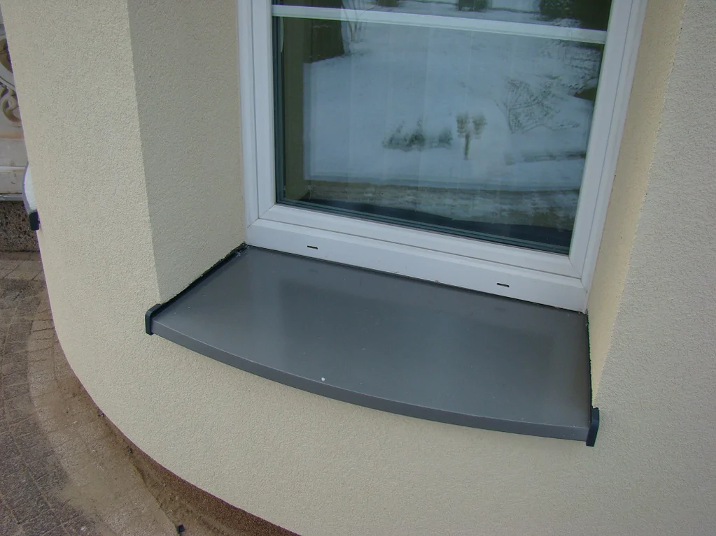 Detal parapetu z blachy na zaokrąglonej elewacji; okno i obróbki blacharskie.