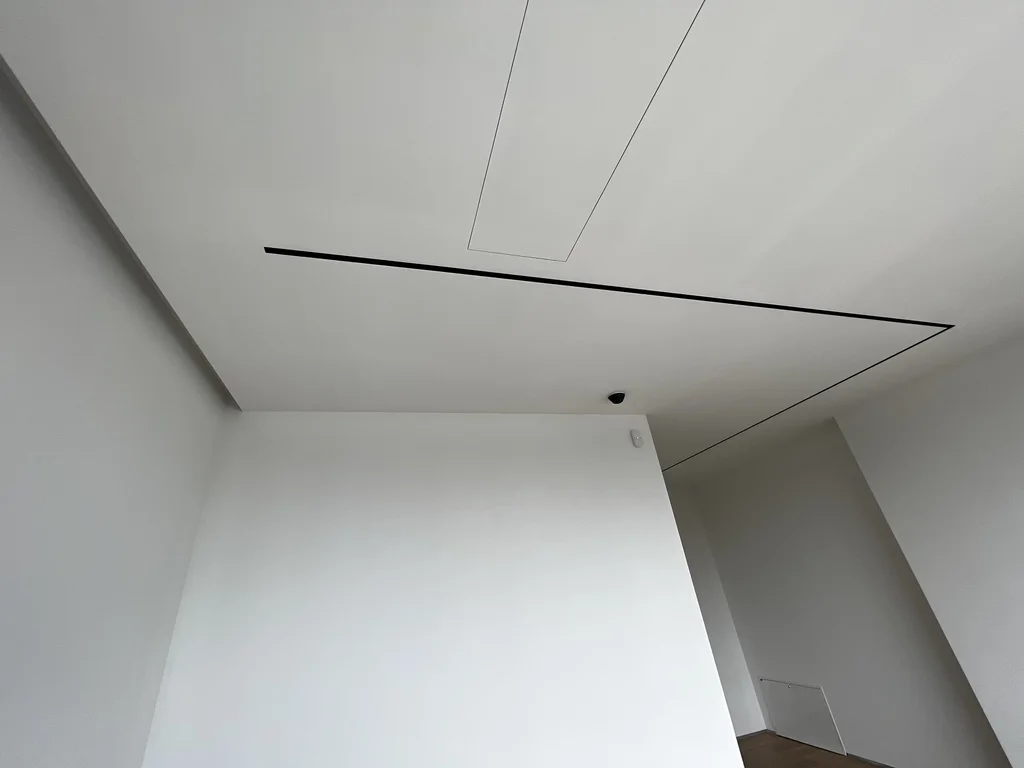 Detal sufitu: długie szczeliny liniowe oraz klapa serwisowa w minimalistycznym wykończeniu.