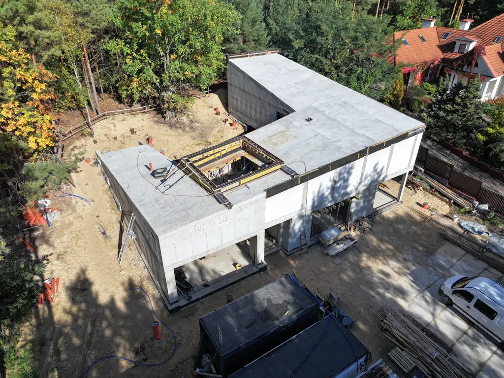 Widok z drona na dom o konstrukcji żelbetowej w trakcie budowy z wewnętrznym patio i pochyłym stropodachem.