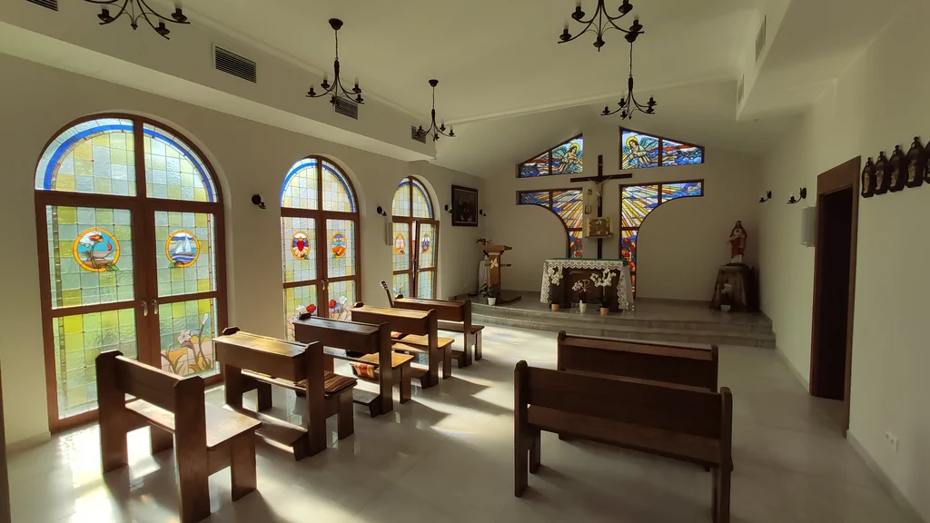 Wnętrze kaplicy w domu zakonnym w Ostródzie, z witrażami, krzyżem i podwyższonym prezbiterium, ławki 