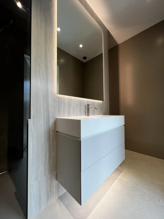 Zbliżenie na podwieszaną szafkę z umywalką i duże lustro z podświetleniem LED.