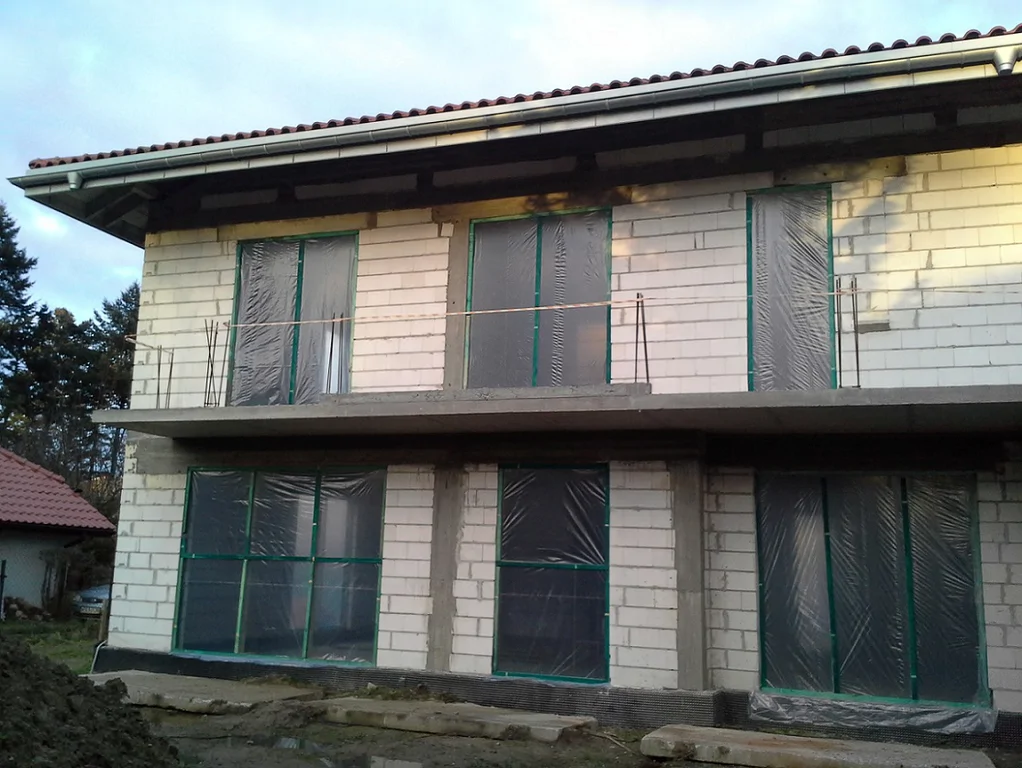 Budowa Domu jednorodzinnego widok z zewnątrz, zaślepione otwory okienne, balkon, wymurowane ściany zewnętrzne