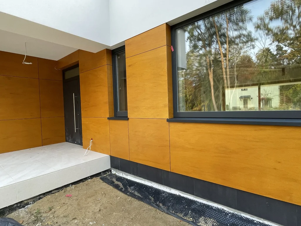 Strefa wejściowa domu w Podkowie Leśnej z dużym oknem i elewacją w kolorze drewna