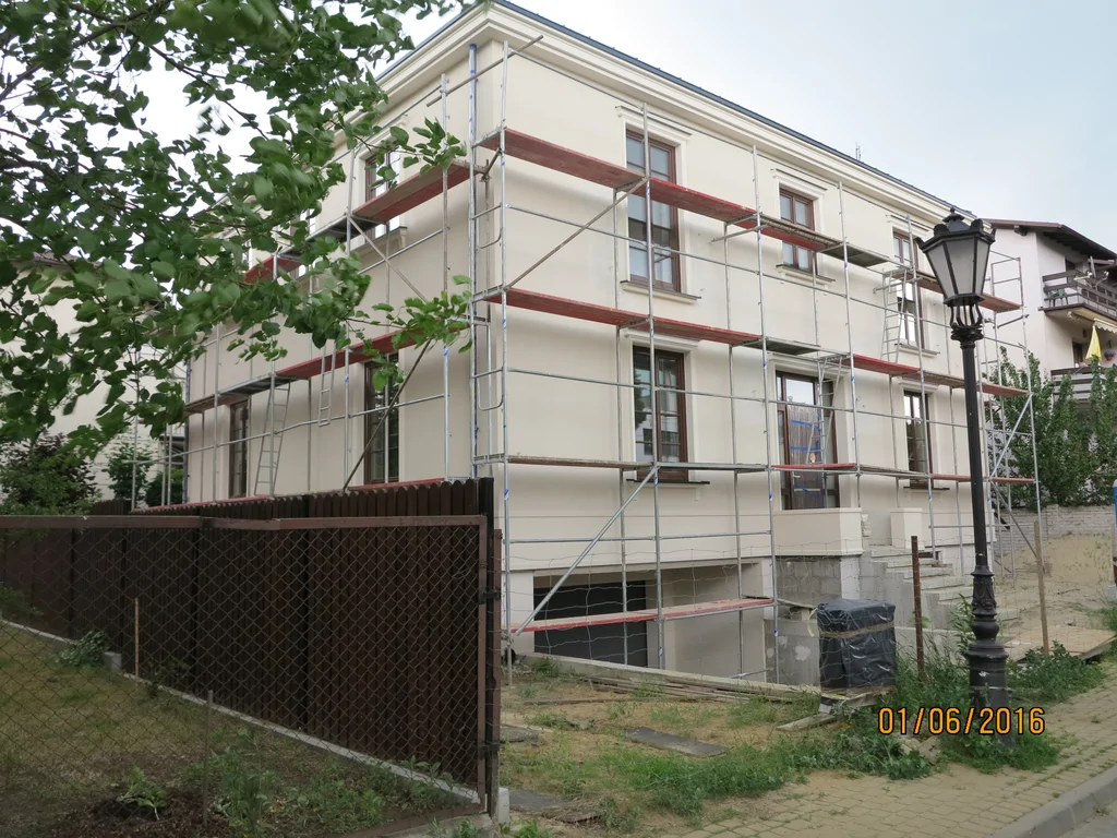 Dom jednorodzinny, biała elewacja, ciemna stolarka okienna, szalunek przy elewacji, lampa