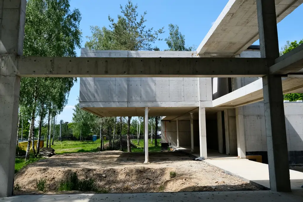 Widok przez otwartą żelbetową ramę budynku na ogród i naturalne otoczenie działki.