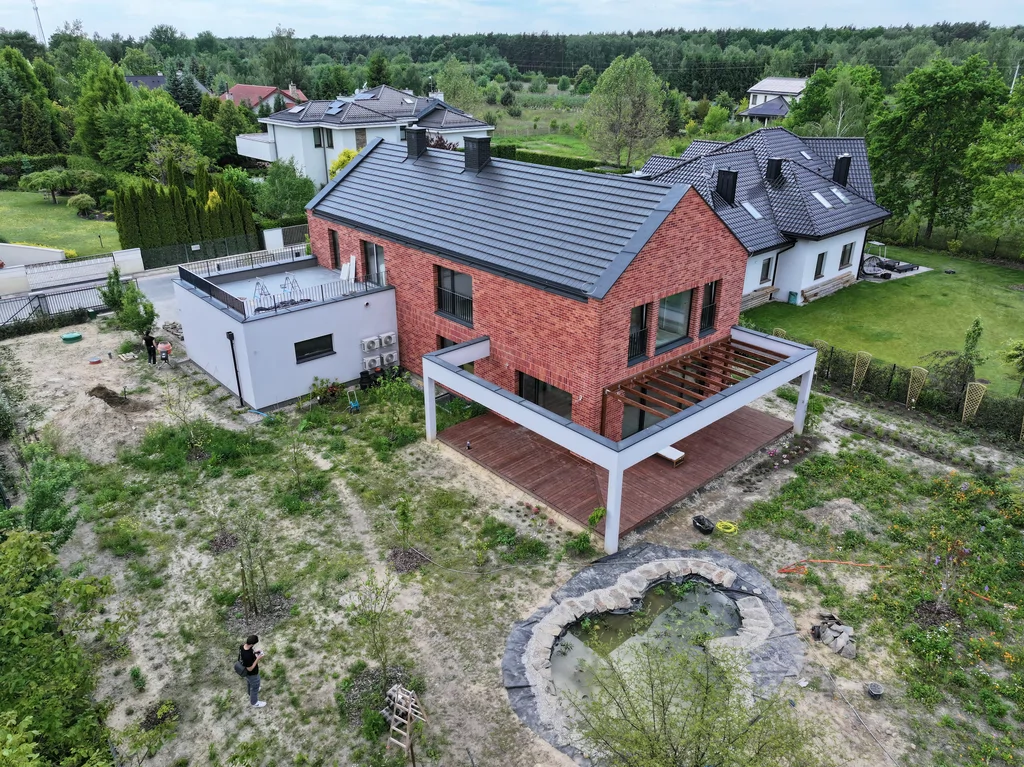 Widok z drona na dom jednorodzinny z tarasem, pergolą oraz oczkiem wodnym w ogrodzie