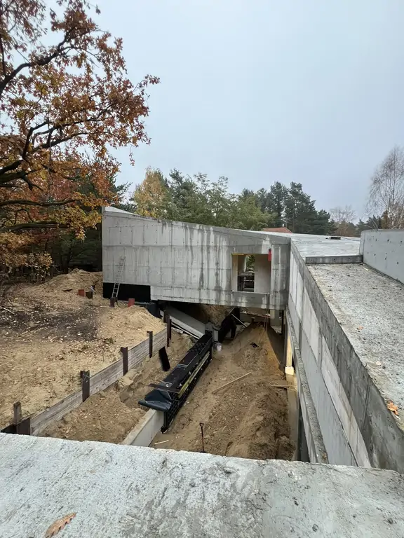 Widok z dachu na żelbetową bryłę domu i zagłębiony dziedziniec w trakcie prac konstrukcyjnych.