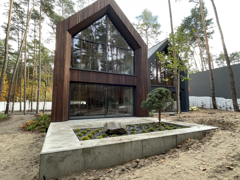 Nowoczesny dom jednorodzinny z drewnianą elewacją, dużym przeszkleniem i minimalistycznym zagospodarowaniem przed elewacją