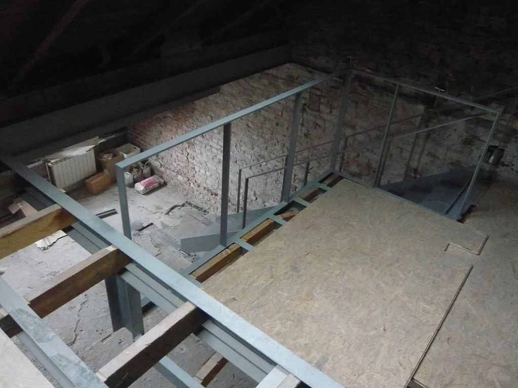 Widok na stalowe schody i ramę antresoli w trakcie montażu, wnętrze w stanie surowym