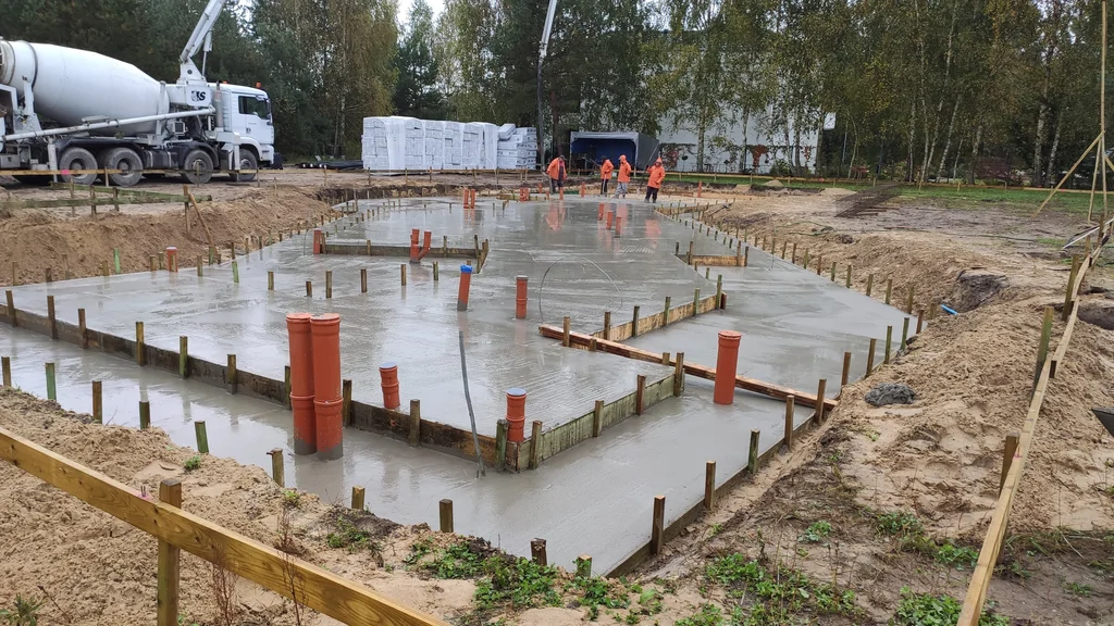 Świeżo wylany chudziak pod płytę fundamentowa z widocznymi przepustami instalacyjnymi i deskowaniem na obwodzie.