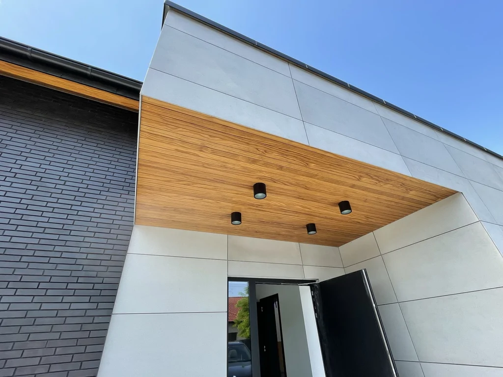 Detal podcienia wejściowego – podbitka drewniana i oprawy sufitowe, okładzina z płyt