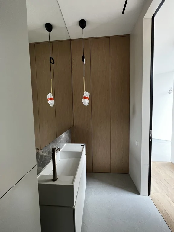 Łazienka z drewnianą ścianą, podwieszanymi lampami i białą zabudową z umywalką.