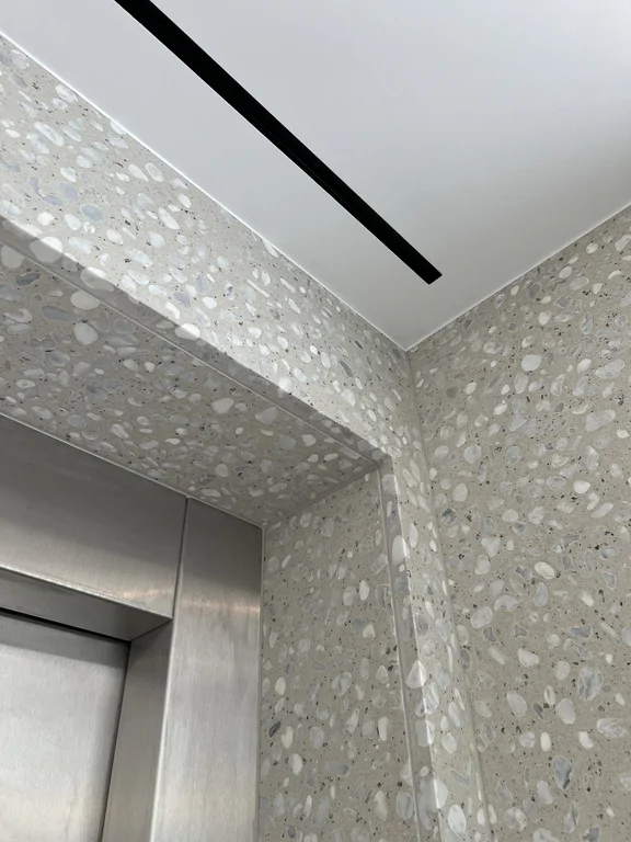 Detal ściany z lastryka przy windzie w nowoczesnym wnętrzu