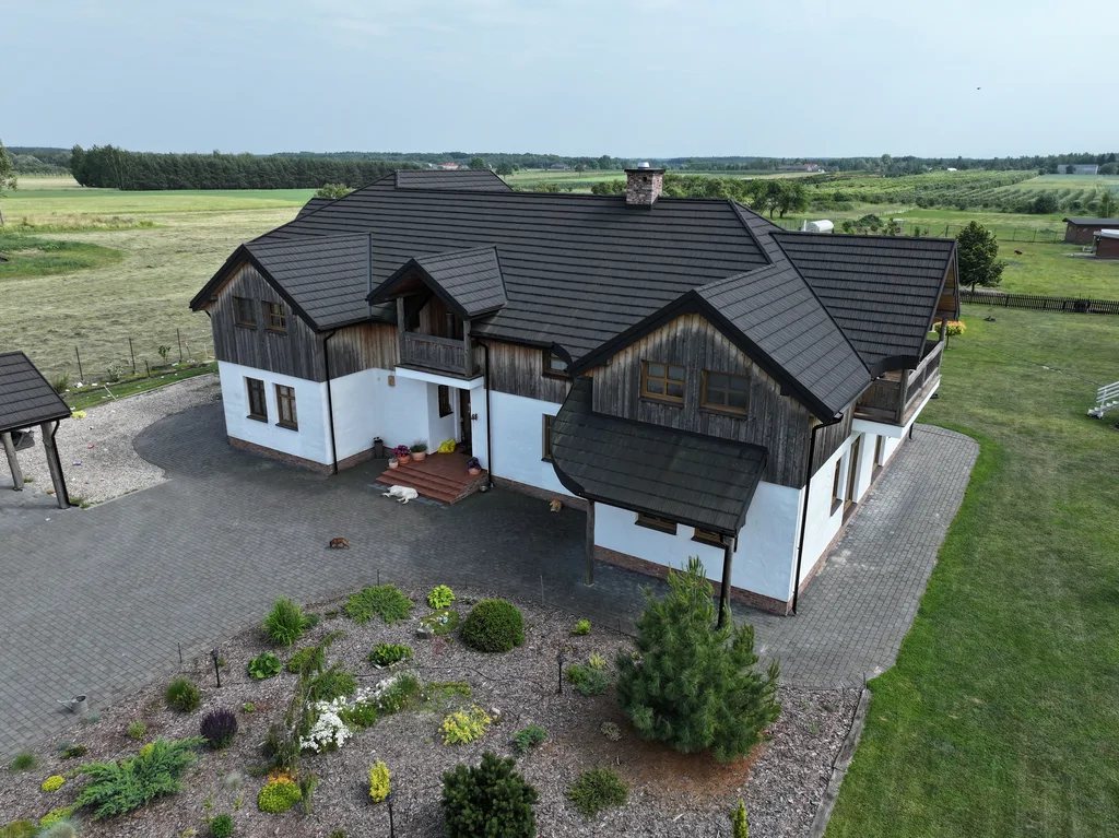 Widok z drona na dom od frontu pod kątem: wejście, zadaszenie oraz ogród z krzewami i rabatami