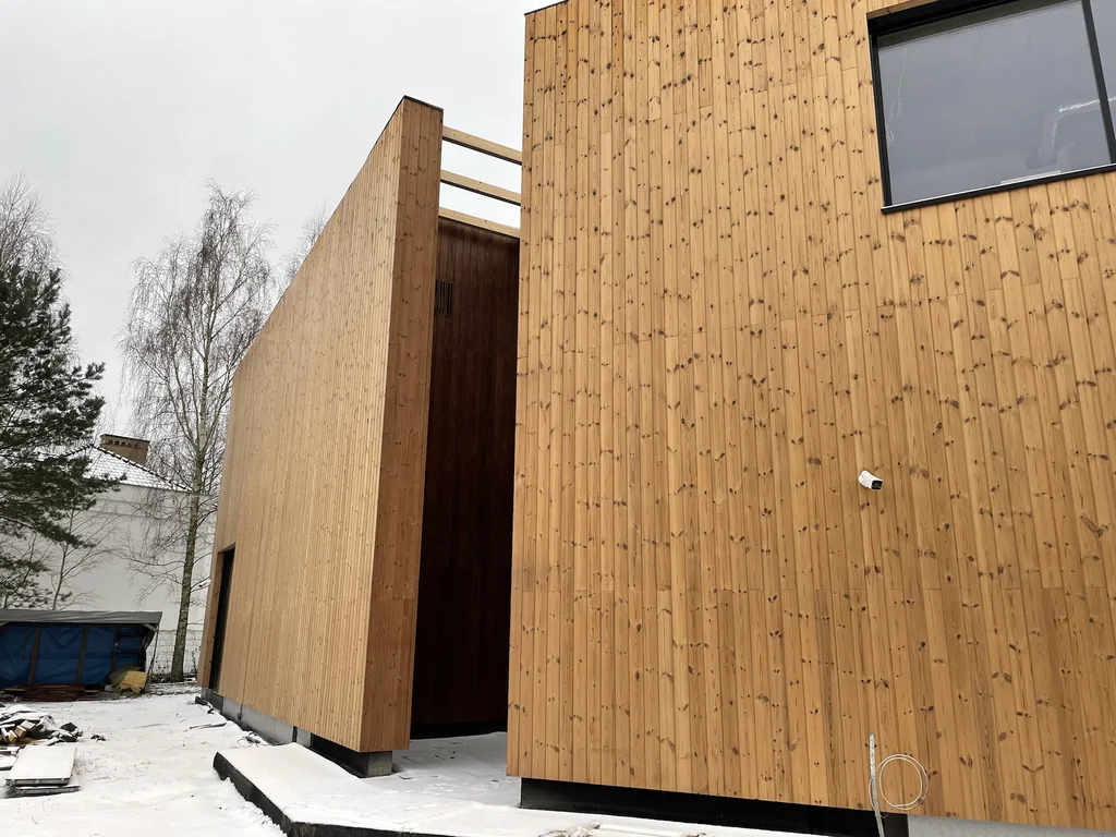 Zimowy widok na bryły obłożone drewnem; wąskie atrium pomiędzy segmentami i detale obróbek przy podstawie elewacji.