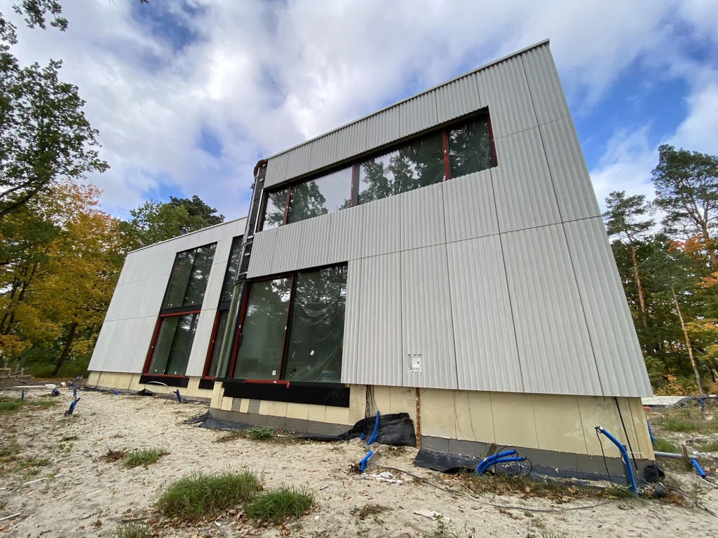 Narożne ujęcie nowoczesnego domu z jasną elewacją, dużymi przeszkleniami i wysokimi oknami na dwóch kondygnacjach