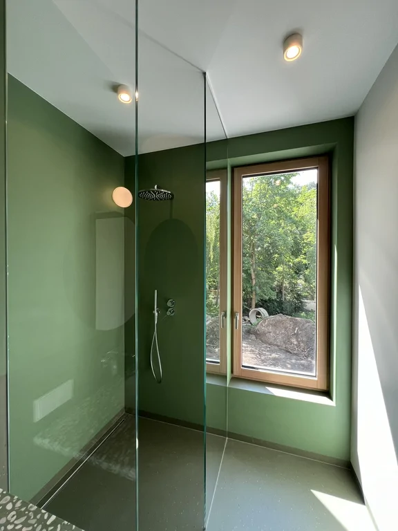 Umywalka z lastrykowym blatem i okrągłym lustrem w zielonej łazience