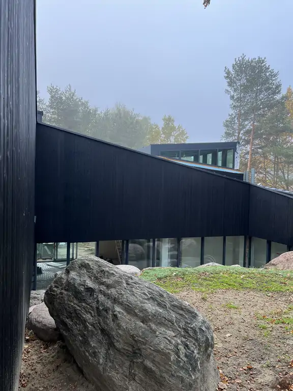 Taras przy nowoczesnym domu z czarną elewacją, wielkoformatowymi płytami i opaską z dużych kamieni naturalnych.