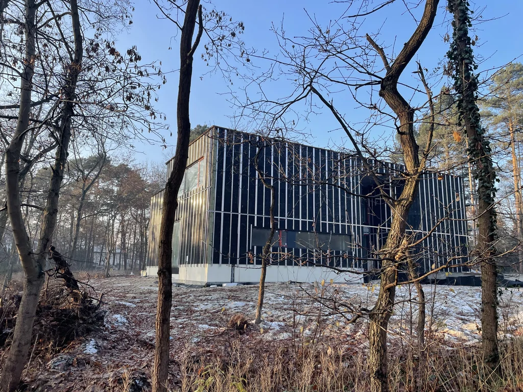 Stan deweloperski nowoczesnego domu z dużymi przeszkleniami, ciemną elewacją i wyraźnym podziałem pionowym