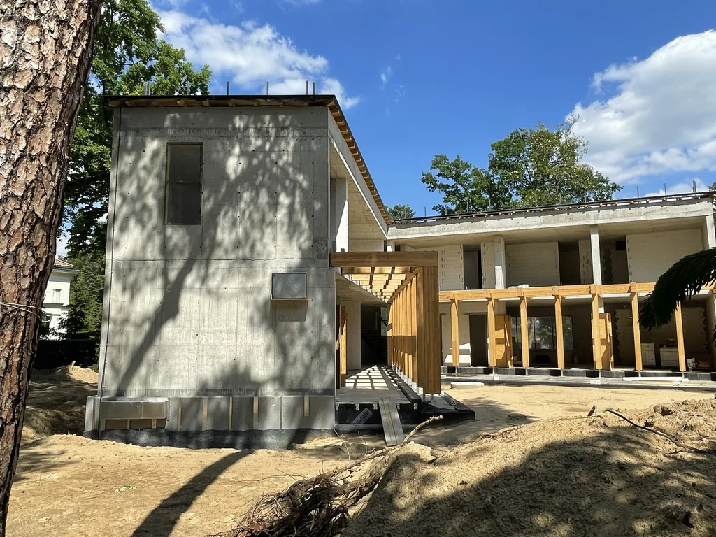 Widok boczny domu z masywną żelbetową bryłą oraz drewnianym zadaszeniem komunikacji przy tarasie