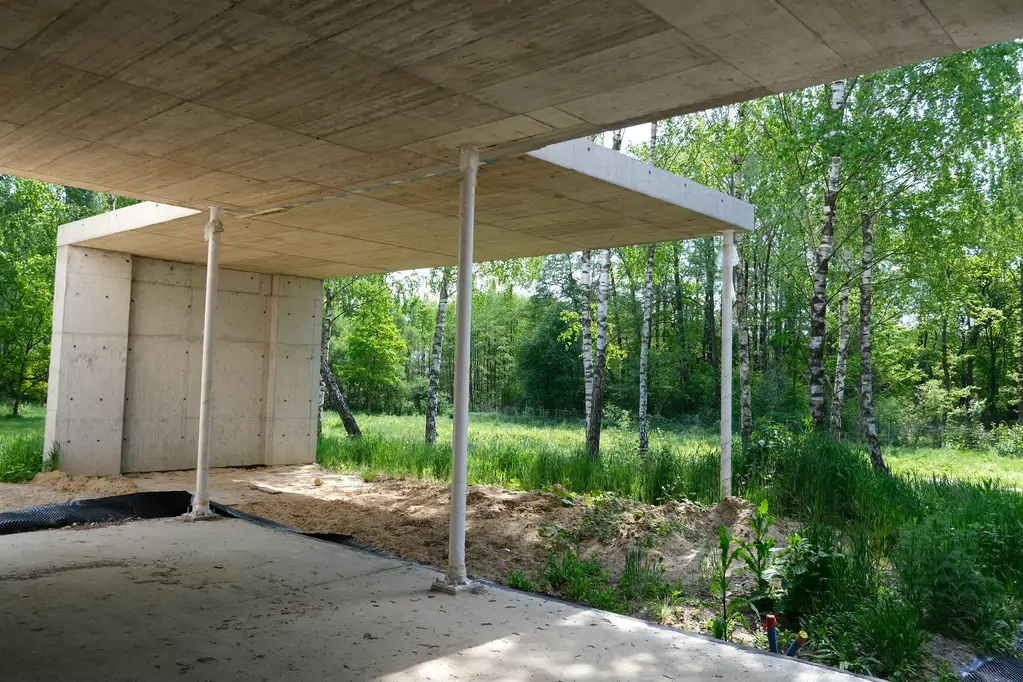 Podcień nowoczesnej willi żelbetowej z widokiem na leśną działkę i otaczającą zieleń.