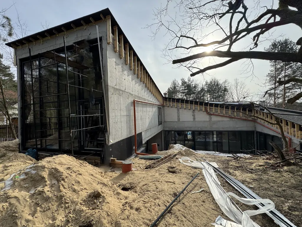 Narożnik nowoczesnego domu z wysokim przeszkleniem, żelbetową elewacją i pochyłym stropodachem.