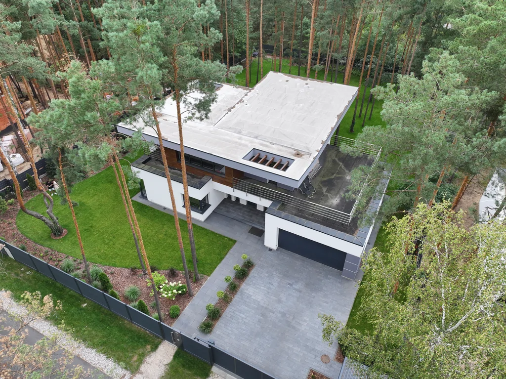 Front domu z drona: podjazd z kostki, brama garażowa i taras na piętrze, ogrodzenie od strony ulicy