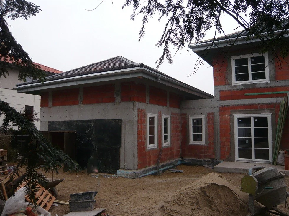  połączenie domu z garażem, plac budowy z betoniarką i materiałami.