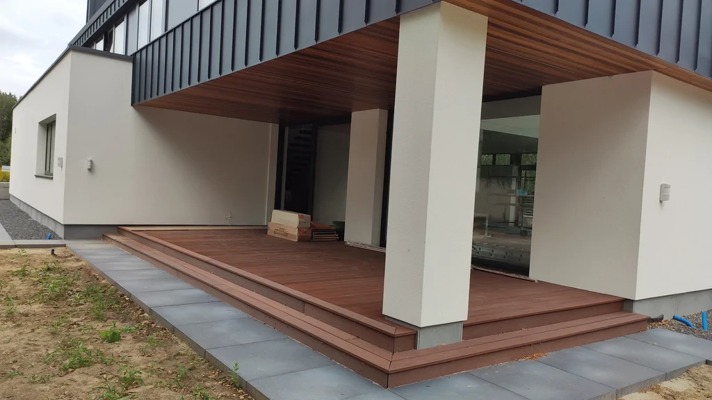 Zadaszony taras nowoczesnego domu z drewnianą deską tarasową i schodami