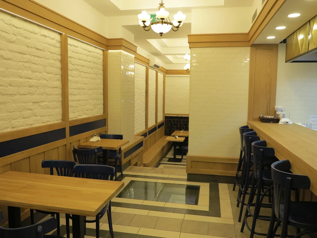 zdjęcie piekarni wewnątrz, stoliki krzesłą, posadzka z podświetlanymi otworami, na ścianach kamień i drewno 