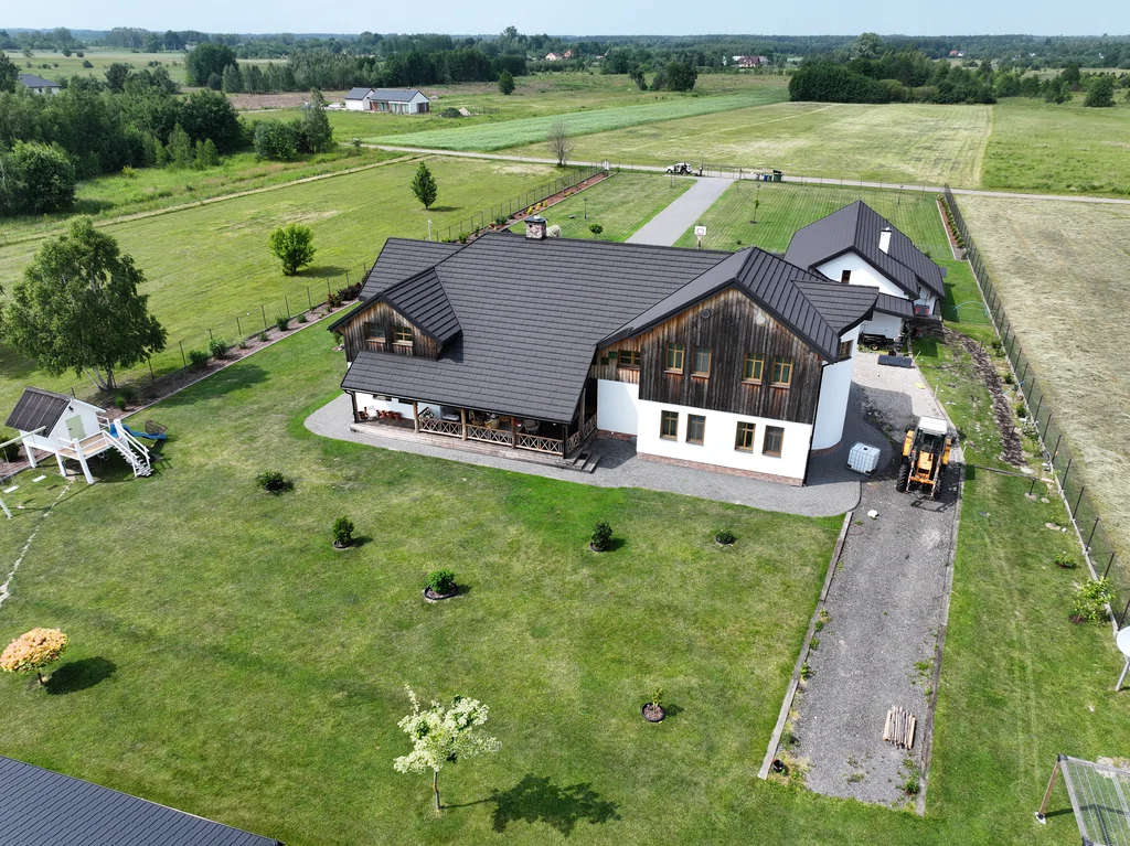 Widok z drona na dom i ogród od strony podwórza; widoczny taras, trawnik oraz budynek garażowy w tle