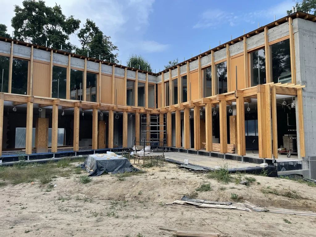 Wewnętrzna elewacja domu jednorodzinnego z wysokimi przeszkleniami i drewnianą pergolą w stanie surowym