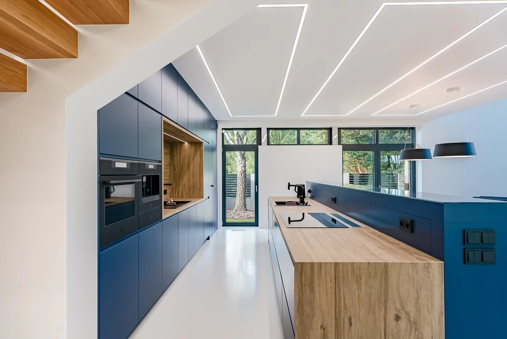 Nowoczesna kuchnia z granatową zabudową, drewnianą wyspą i dużymi przeszkleniami.