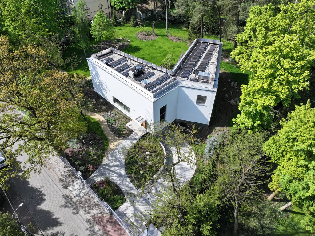 Widok z lotu ptaka na frontową część posesji z zakrzywionym podjazdem, białą bryłą domu i zielonym ogrodem